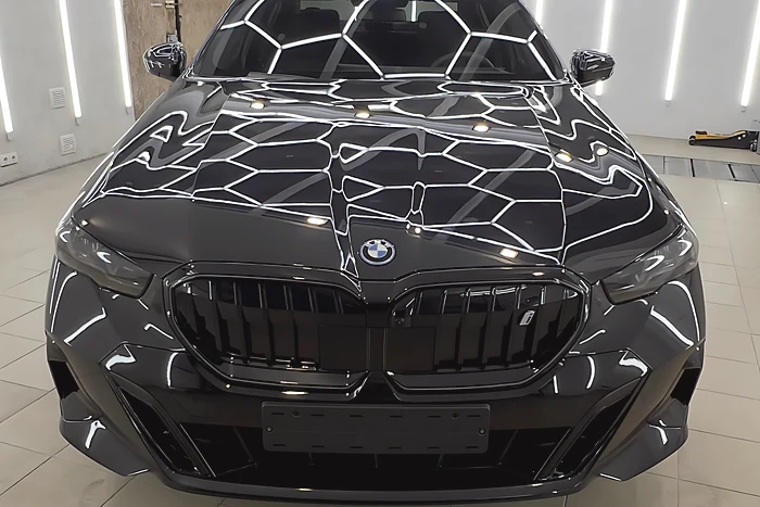 Juodas BMW i5 iš priekio: kapote šešiakampio apšvietimo atspindys